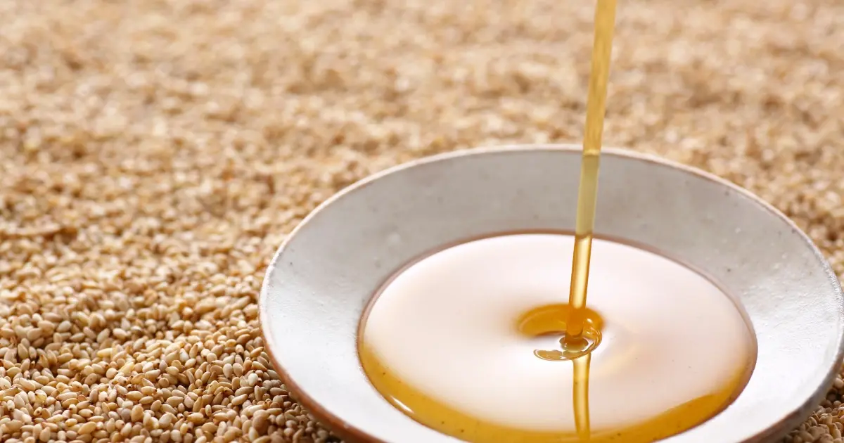 روغن کنجد در ظرف شیشهای با دانههای کنجد اطراف آن