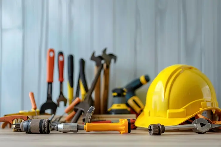 ابزارهای ساختمانی مختلف مانند چکش، برس و کفش کارگری در کنار یک محیط ساختوساز