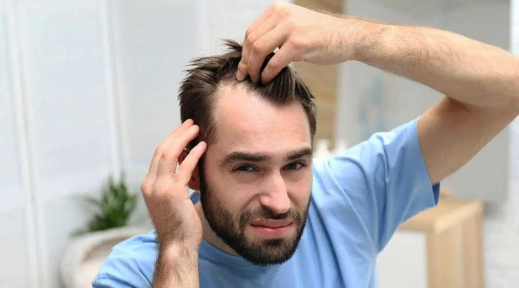 مردی که با نگرانی به موهای خود نگاه میکند و نشاندهنده ریزش مو است